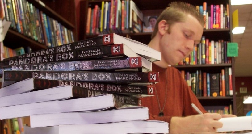 Nathan J.S. Marchand author with pile of copies of his book Pandora's Box