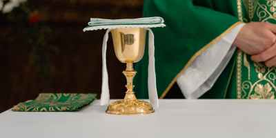 golden chalice on table beside a priest in green chasuble