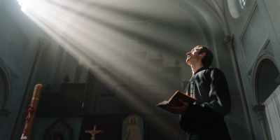 sunrays passing through a church window beside a priest holding a bible
