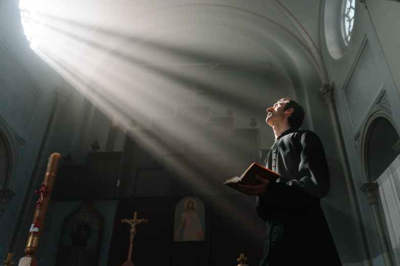sunrays passing through a church window beside a priest holding a bible