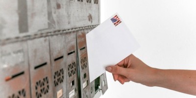 Person's hand putting letter into post office box to illustrate poem "An Envelope is its Own Story" by Lawrence Hall. Photo Credit: Element5 Digital/Pexels https://www.pexels.com/photo/person-holding-white-envelope-1550334/