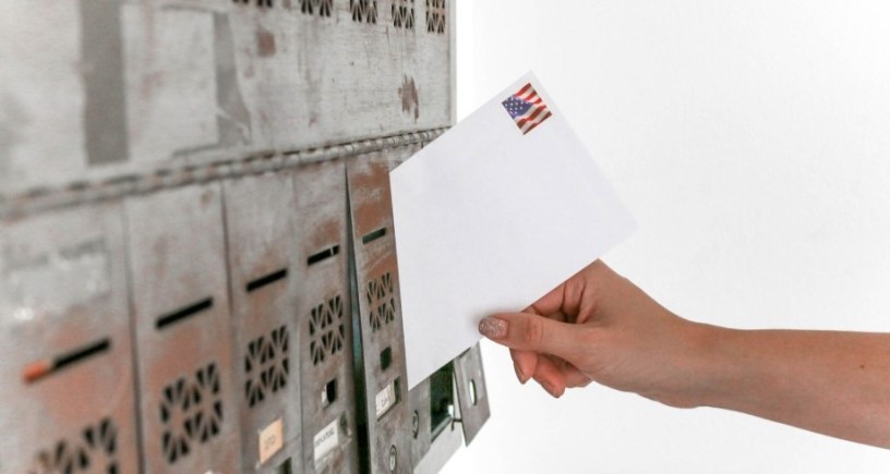 Person's hand putting letter into post office box to illustrate poem "An Envelope is its Own Story" by Lawrence Hall. Photo Credit: Element5 Digital/Pexels https://www.pexels.com/photo/person-holding-white-envelope-1550334/